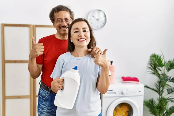 Średniego Wieku Międzyrasowe Para Robi Pranie Trzymając Butelkę Detergentu Uśmiechnięty — Zdjęcie stockowe