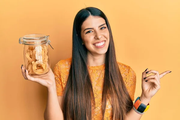 Junge Hispanische Frau Hält Glas Mit Ungekochten Nudeln Und Lächelt — Stockfoto