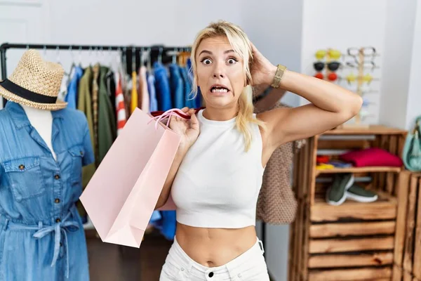 年轻的高加索女人在零售店疯狂地拿着购物袋 双手放在头上吓得直哆嗦 吓得张大了嘴 吓了一大跳 — 图库照片