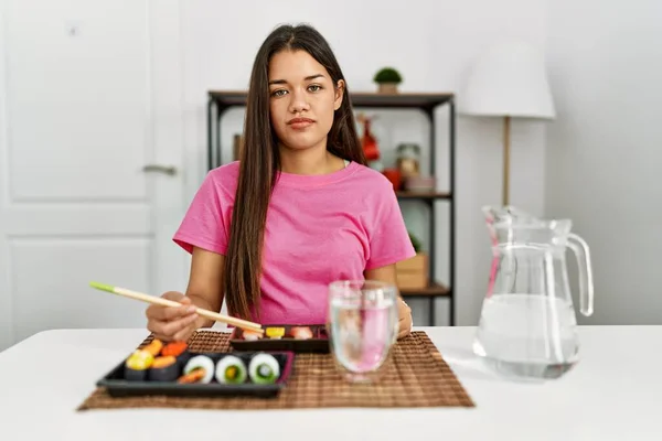 若いブルネットの女性が顔に深刻な表情でリラックス箸を使用して寿司を食べています カメラを見ているだけで — ストック写真
