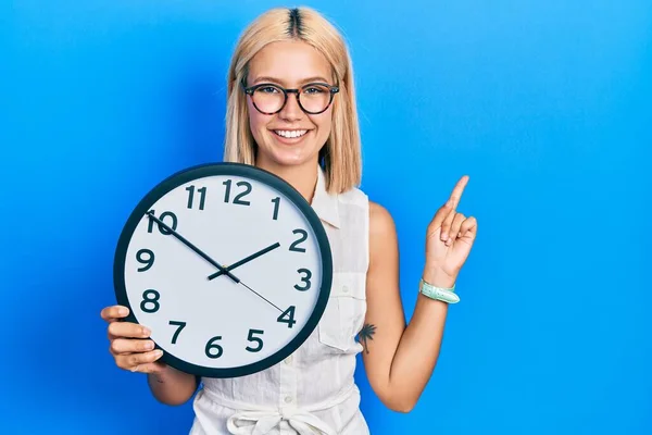 Hermosa Mujer Rubia Sosteniendo Gran Reloj Sonriendo Feliz Señalando Con —  Fotos de Stock