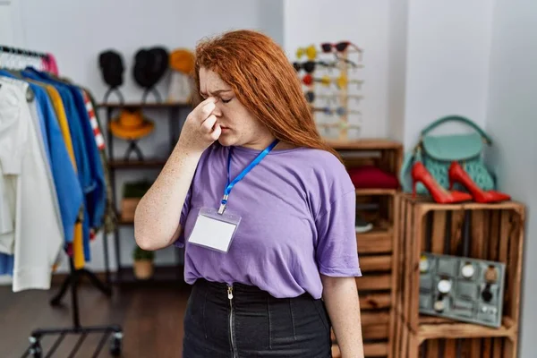 Young redhead woman working as manager at retail boutique tired rubbing nose and eyes feeling fatigue and headache. stress and frustration concept.