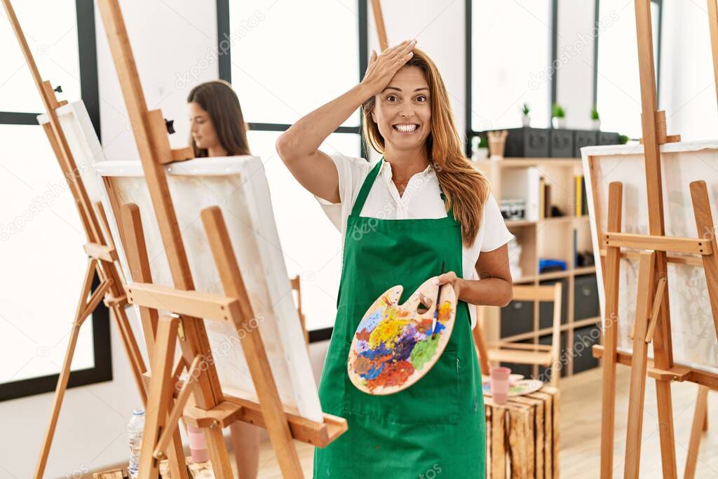 Young hispanic middle age woman at art classroom stressed and frustrated with hand on head, surprised and angry face 