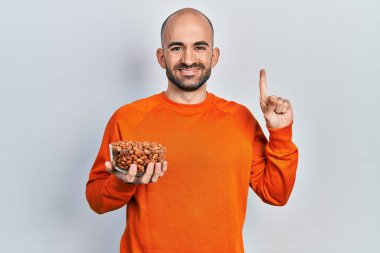 Elinde fıstıkla gülümseyen genç kel bir adam bir fikir veya soru işareti ile mutlu bir yüzle, bir numara 