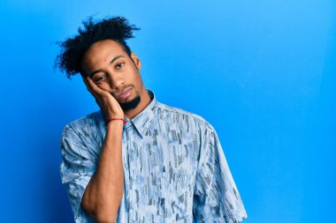 Sakallı, sıradan giyinmiş, depresyondan sıkılmış ve yorgun görünen, kollarını kavuşturmuş genç Afrikalı Amerikalı bir adam.. 