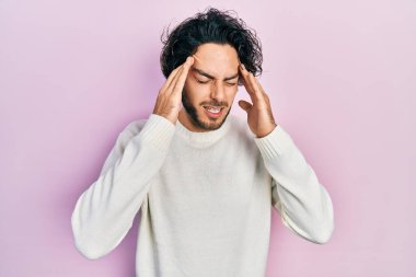 Yakışıklı, beyaz kazak giyen, elleri kafasında, stresten baş ağrısı çeken bir İspanyol. migren ağrısı. 
