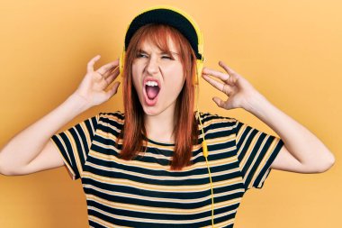 Kızıl saçlı, müzik dinleyen genç bir kadın. Öfkeli ve öfkeli çığlıklar atan, öfkeyle bağıran kulaklıklar takıyor. öfke ve agresif konsept. 