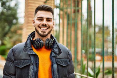 Sakallı yakışıklı, neşeli ve kendine güvenen, kışlık palto ve kulaklık takan bir İspanyol.