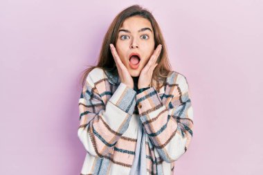 Kafkasyalı genç bir kız günlük kıyafetler giyiyor. Korkmuş ve şok olmuş, şaşırmış ve şaşırmış bir yüz ifadesi var. 