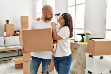 Genç İspanyol çift mutlu bir şekilde gülümsüyor. Yeni evinde karton kutu tutuyorlar..