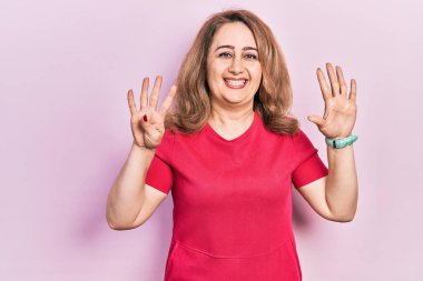 Orta yaşlı beyaz kadın, günlük kıyafetler giyip dokuz numaralı parmaklarıyla işaret ederken kendinden emin ve mutlu bir şekilde gülümsüyor.. 