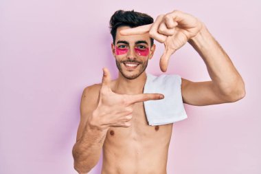 Havlu ve göz torbaları takmış, gülümseyen, elleri ve parmakları gülen yüzlü İspanyol bir adam. yaratıcılık ve fotoğrafçılık kavramı. 