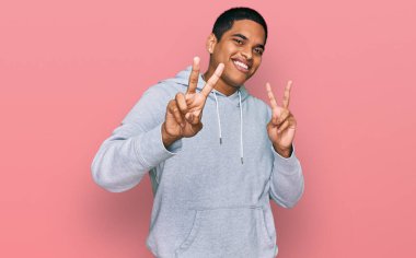 Gündelik kazak giyen genç, yakışıklı İspanyol adam kameraya bakıp zafer işareti yapıyor. İki numara.. 