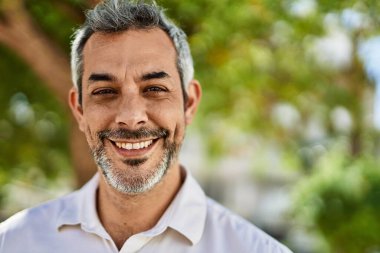 Orta yaşlı, kır saçlı, gülümseyen bir adam şehirde mutlu bir şekilde duruyor..