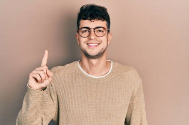 Gündelik kıyafetler giyen ve gözlüklü genç İspanyol bir numarayı gösterip işaret ederken kendinden emin ve mutlu bir şekilde gülümsüyor.. 