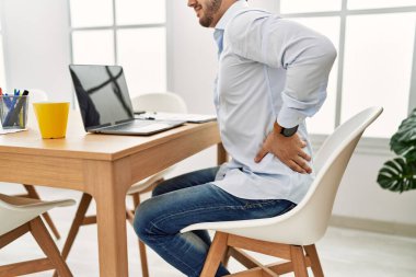 Ofiste çalışan genç İspanyol işadamı. Sırt ağrısıyla masada oturmak.