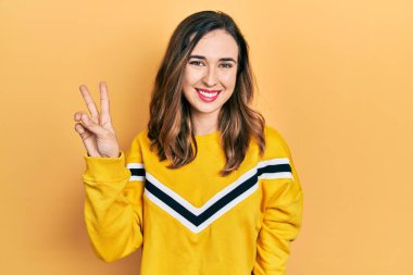 Gündelik kıyafetler giyen genç İspanyol kız kameraya bakıp zafer işareti yaparken parmaklarını gösteriyor. İki numara.. 
