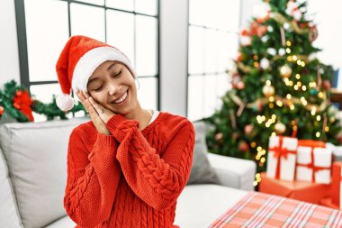 Kısa saçlı, ispanyol bir kadın Noel şapkası takıyor, koltukta uyuyor, yorgun yatıyor, hayal kuruyor, elleriyle poz veriyor, gözleri kapalı gülümsüyor.. 