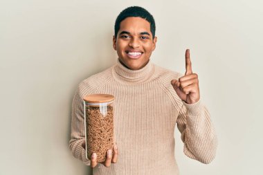 Genç, yakışıklı İspanyol adam elinde sağlıklı tahıllı mısır gevreği kavanozu tutarken bir fikir veya soru işareti ile gülümsüyor. 