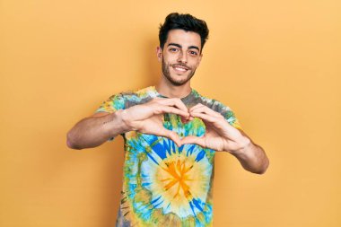 Gündelik kıyafetler giyen, aşık gülümseyen, elleriyle kalp sembolü yapan genç bir İspanyol. romantik kavram. 