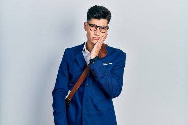 İş kıyafetleri giymiş genç İspanyol bir adam diş ağrısı ya da diş hastalığından dolayı acı dolu bir ifadeyle ağıza dokunuyor. dişçi 