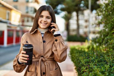 Genç, güzel, esmer bir kadın dışarıda mutlu bir şekilde gülümsüyor telefonda konuşuyor.