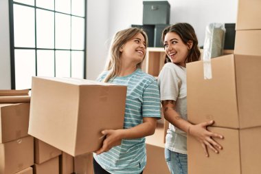 Mutlu bir şekilde gülümseyen genç çift yeni evlerinde karton kutular tutuyor..