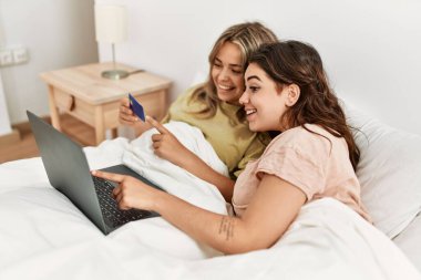 Yatak odasında kredi kartı ve laptop kullanan genç bir çift.