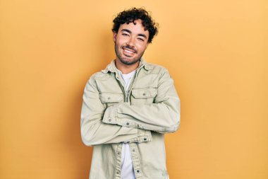 Gündelik kıyafetler giyen, kollarını kavuşturup kameraya gülümseyen genç İspanyol adam. pozitif kişi. 