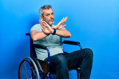 Yakışıklı, orta yaşlı, gri saçlı, tekerlekli sandalyede oturan, reddedilmiş, kollarını kavuşturup negatif işaret veren, kızgın yüzlü bir adam. 