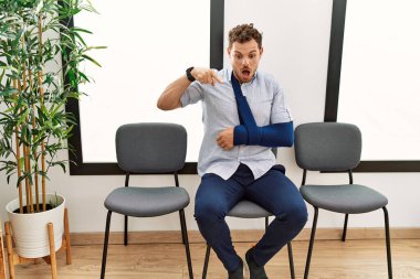 Yakışıklı genç adam, doktor bekleme odasında oturuyor. Kolundan yaralanmış, parmaklarını göstererek reklamını yapıyor. Şaşırmış yüz ifadesi ve ağzı açık. 