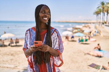Genç Afrikalı Amerikalı kadın sahilde akıllı telefon kullanıyor..