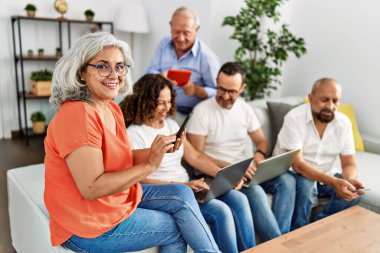 Bir grup orta yaşlı arkadaş dizüstü bilgisayar ve akıllı telefon kullanarak evdeki kanepede oturuyorlar..