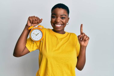 Genç Afrikalı Amerikalı kadın elinde çalar saatle gülümsüyor bir fikir ya da soru işareti ile mutlu bir yüzle, bir numara 