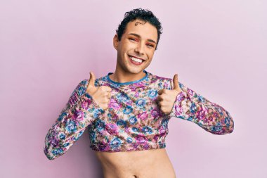 Makyaj elbisesi giyen yakışıklı bir adam. Başarı işareti yapıyor. Elinde olumlu bir jest yapıyor. Neşeli ifade ve kazanan jest. 