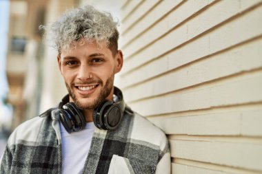 Şehirde kulaklık takarak mutlu gülümseyen genç İspanyol adam..