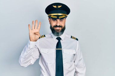 İspanyol asıllı genç adam uçak pilotu üniforması giyiyor. Dört numarayı gösterip işaret ederken kendinden emin ve mutlu bir şekilde gülümsüyor.. 
