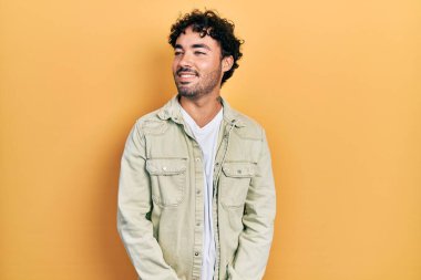 Gündelik kıyafetler giyen genç İspanyol bir adam yüzünde gülümsemeyle yan yana bakıyor, doğal bir ifade. Kendinden emin gülen. 