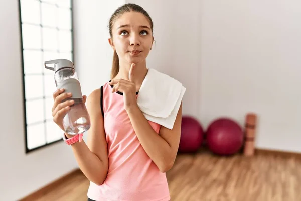 Joven Adolescente Morena Con Ropa Deportiva Sosteniendo Botella Agua Pensando —  Fotos de Stock