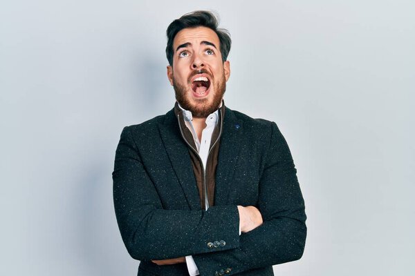 Красивый белый мужчина с бородой и скрещенными руками, злой и безумный, кричащий расстроенный и разъяренный, кричащий от гнева, глядя вверх. 