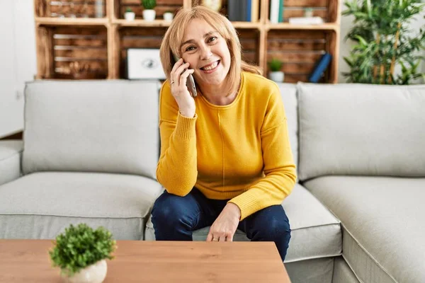 Middelbare Leeftijd Blonde Vrouw Praten Smartphone Zitten Bank Thuis — Stockfoto