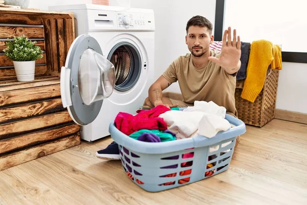 年轻英俊的男人把脏衣服放进洗衣机里 不停地用手掌唱歌 用消极而严肃的手势警告人 — 图库照片