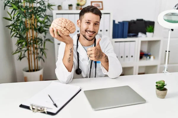 Jovem Médico Segurando Cérebro Clínica Médica Sorrindo Feliz Positivo Polegar — Fotografia de Stock