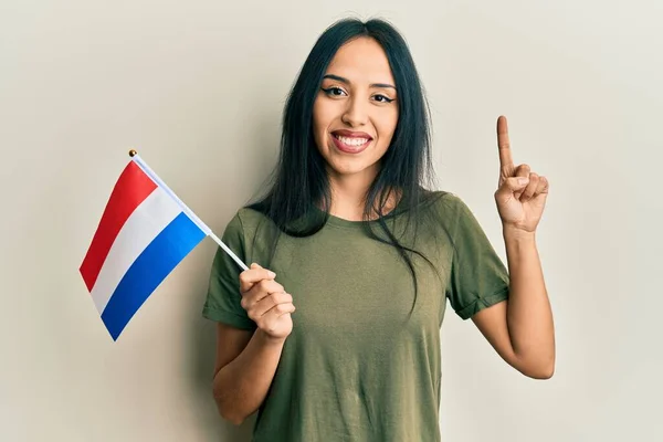 年轻的惊慌失措的女孩举着荷兰国旗微笑着 带着一个想法或问题 满脸喜形于色 指手画脚 位居第一 — 图库照片