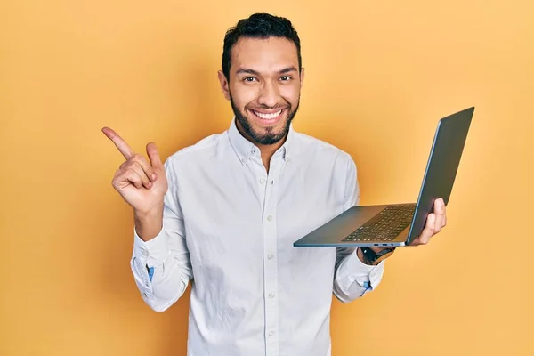 一个留着胡子的西班牙男人用电脑笔记本电脑微笑着 手指手画脚地朝旁边看去 — 图库照片