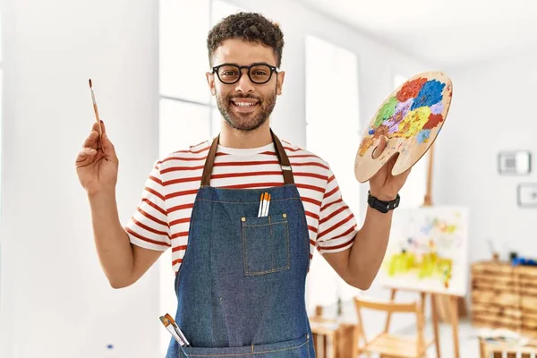 Jovem Artista Árabe Homem Sorrindo Feliz Segurando Pincel Paleta Estúdio — Fotografia de Stock