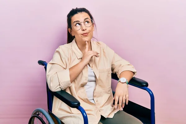 車椅子に座っている若いヒスパニック系の女性は 顎に指で疑いに集中し 疑問を見上げ — ストック写真