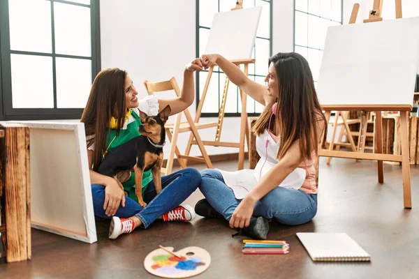 二人のラテンペイント学生笑顔幸せなバンプ拳で床に座って犬とともにアートスクール — ストック写真