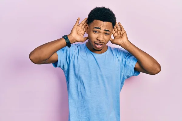 若いアフリカ系アメリカ人の男性は 耳のジェスチャーで両方の手を聞くしようとしてカジュアルな青のTシャツを着て ゴシップを好奇心 聴覚障害や聴覚障害 — ストック写真