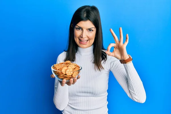 Young Hispanic Woman Holding Salty Biscuits Bowl Doing Sign Fingers — Stock Photo, Image